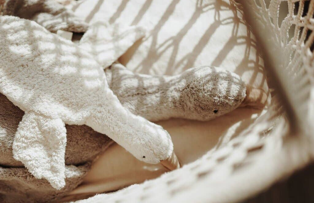 White plush toy resembling a duck on a textured surface with soft lighting