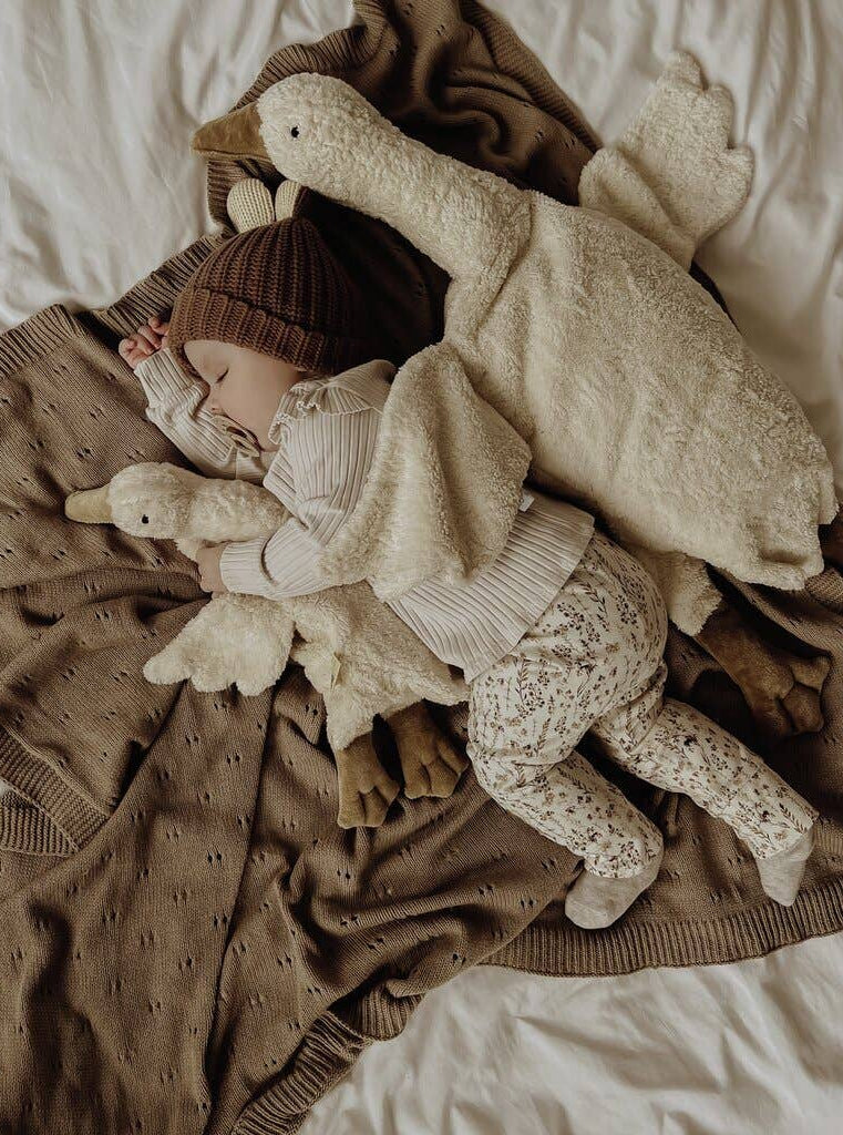 Child wrapped in a blanket with plush toys on a bed